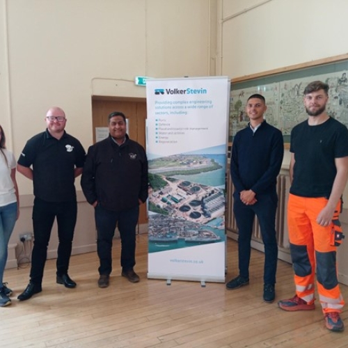 People smiling stood next to a VolkerStevin banner. 