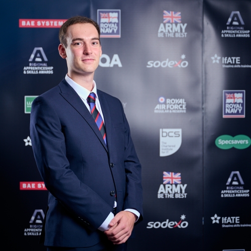 Photo of Adam Parkinson in a suit and tie stood in front of black banner with logos on