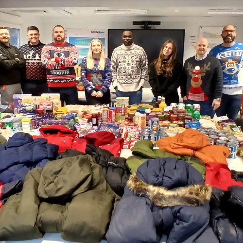 7Men and women stood in front of a table with clothing on all wearing Christmas jumpers