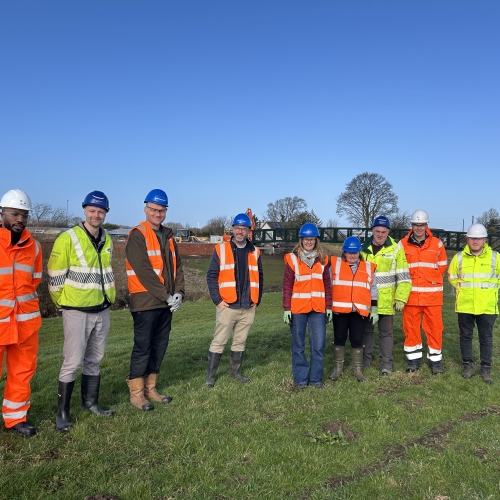 Group of men and women in Hi-vis workwear stood in a field with blue skies