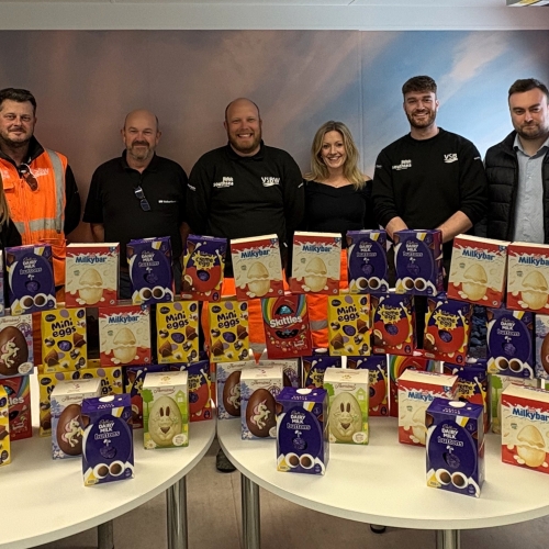 Men and women stood behind a table in an office with Easter eggs on the table