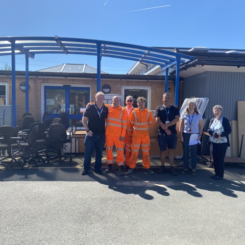 Group of men and women stood outside a school with furniture with bright blue skies