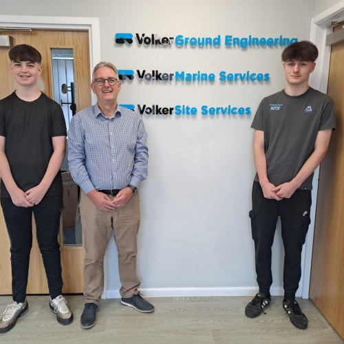 Three men stood in front of a white wall with three logos on the wall behind them