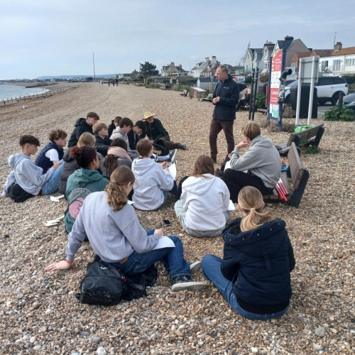 Students listening to a talk on a pebble beach.