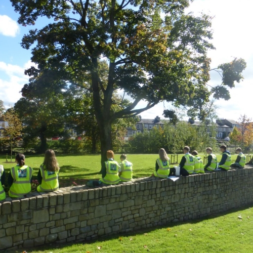 Group of school students in hi-vis sat on a wall looking out towards a field