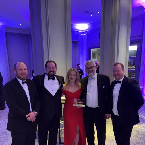 four men in black tie and one women in a red dress stood together with a glass trophy