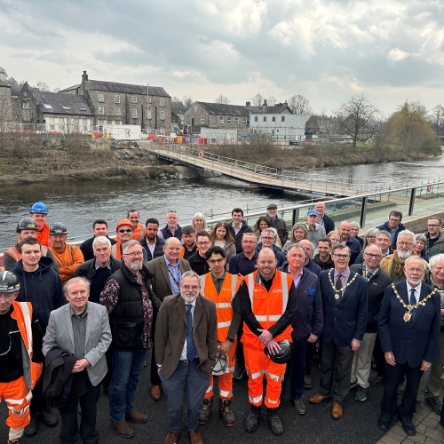 Group of men and women some in orange hi-vis workwear stood on a bridge with a river behind