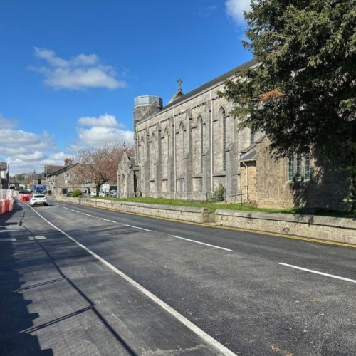 road and flood wall to the left and houses to the right. Bright blue skies