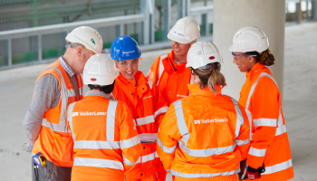 Group of six people all wearing orange PPE, stood talking/looking at each other