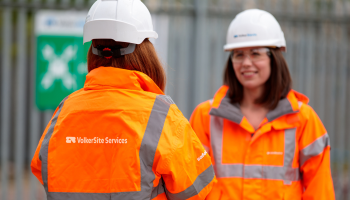 Two women in orange PPE and white hard hats