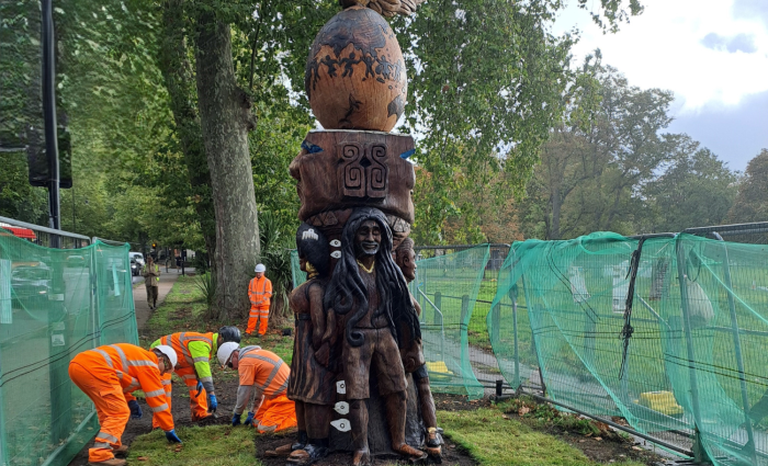 Construction workers laying new turf at the bottom of a totem pole.