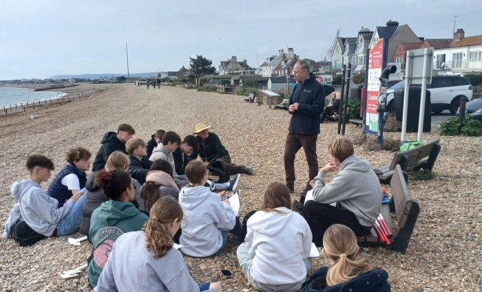Students listening to a talk on a pebble beach.