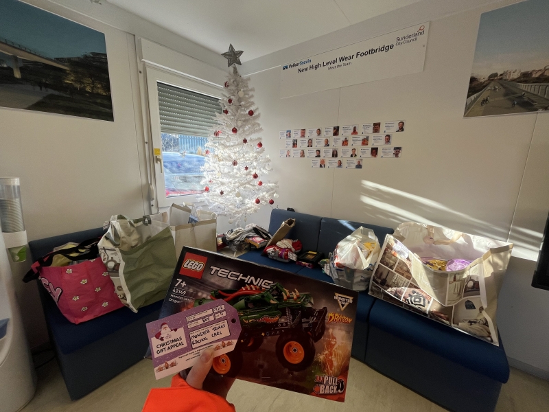 Picture of a white Christmas tree in the corner of an office with presents around it