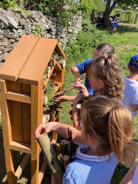 Young children putting logs into a wooden bug house