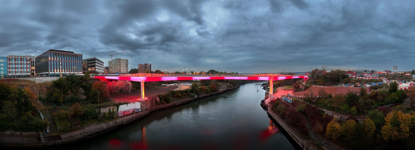 Aerial view of Kell Crossing footbridge lit up at night in red and white along the side of the bridge