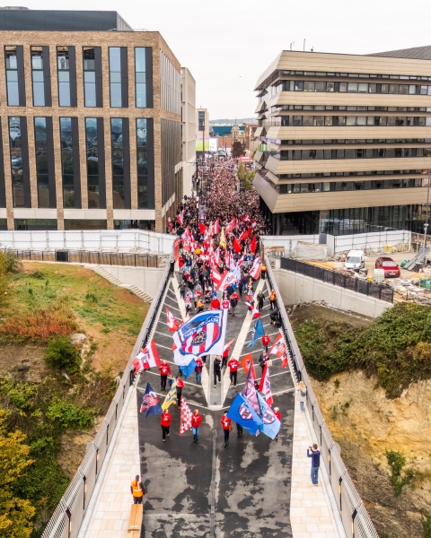 Keel Crossing opening - people walking across a bridge with red and white flags