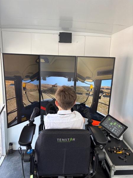 school boy sat in charge in front of three screens on a digger stimulator