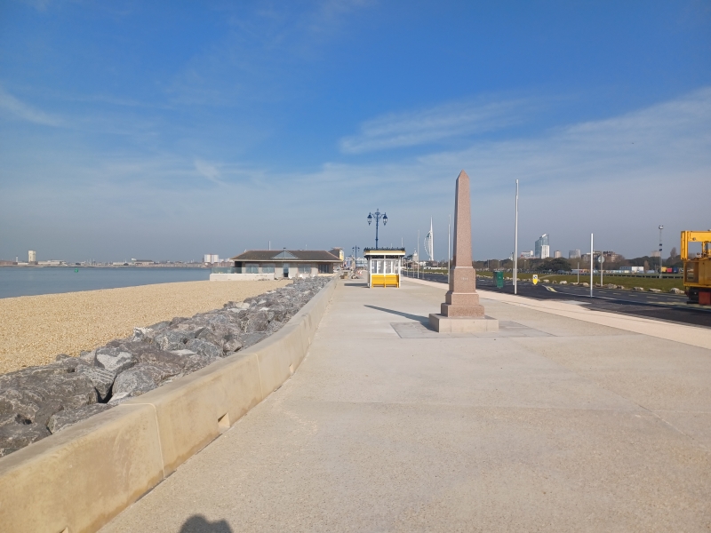 Promenade with promenade wall to the left. a monument and yellow ornate shelter in the background