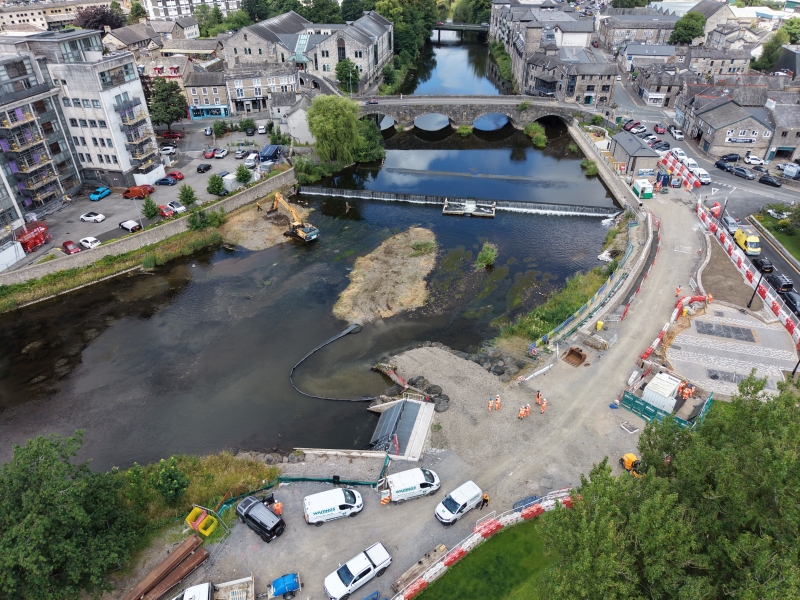 aerial photo of construction in the river with a bridge in the background and construction site on the banks