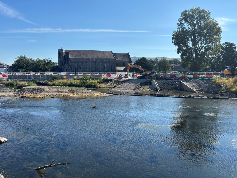 River in the foreground and construction work taking place in the background on the bank of the river