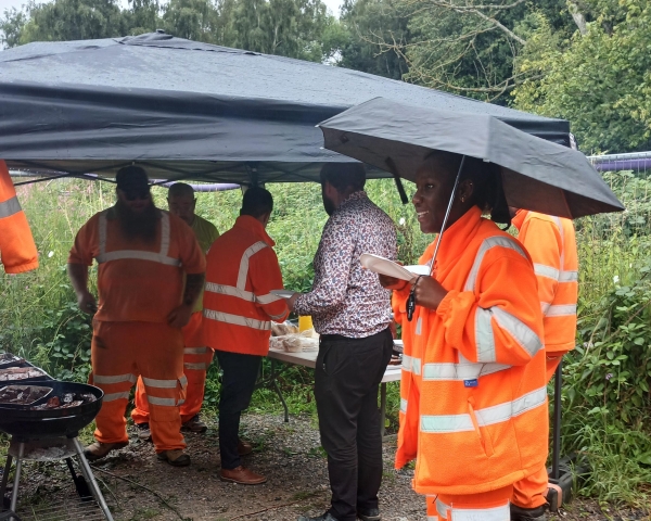 People in orange high vis cooking a BBQ outside in the rain.