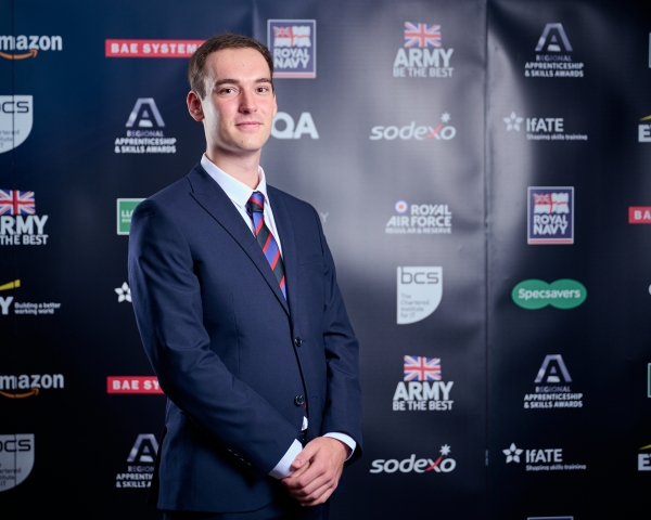 Photo of Adam Parkinson in a suit and tie stood in front of black banner with logos on
