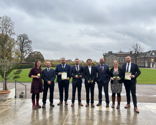A group of eight men and women holding two certificates and two trophies
