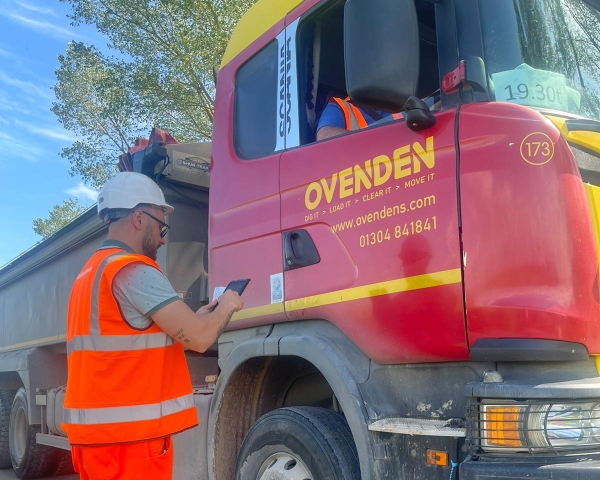 Picture of a man stood near a lorry on his phone.