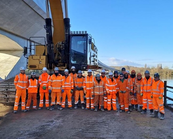 Group photo of men and women in orange hi vis workwear in front of a piece of construction equipment