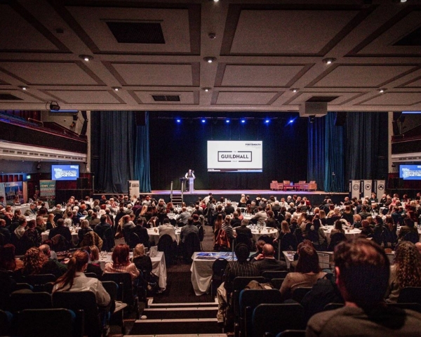 an auditorium filled with people facing a stage with a large screen on the stage