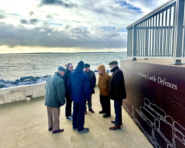 A group of male retired engineers stood by fencing on Southsea promenade