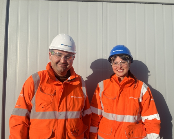 Photo of man and women stood against white building in orange hi-vis workwear