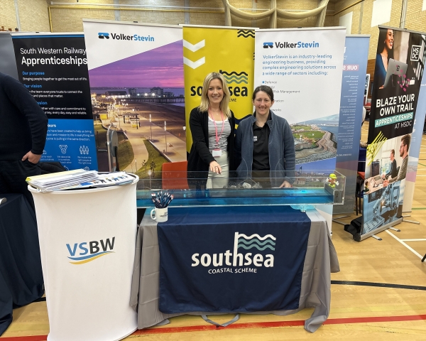 Two women stood behind a table with banners behind them 