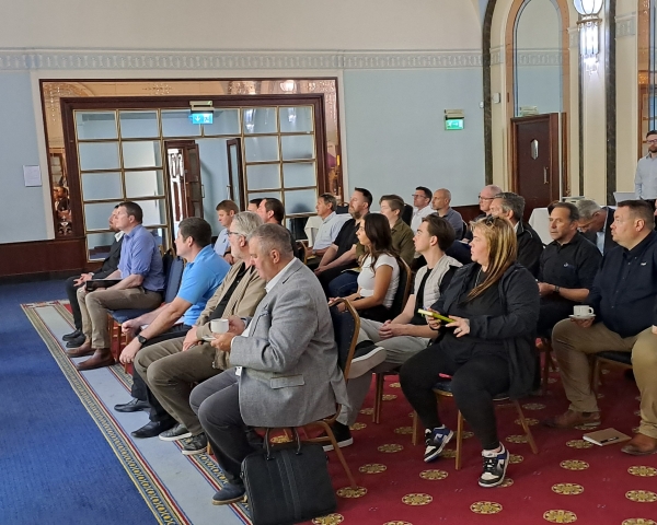 Room of people sat being presented to with slides on a  large screen