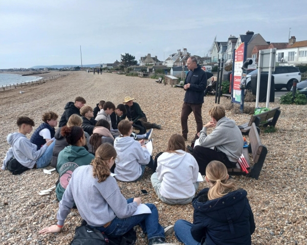 Students listening to a talk on a pebble beach.