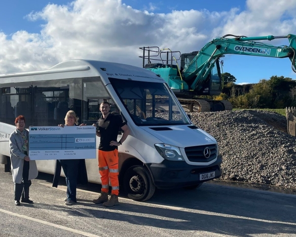 People with a giant check stood in front of a bus.