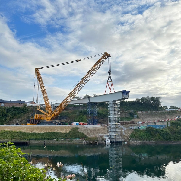Crane lifting a section of the bridge into place on a sunny day.