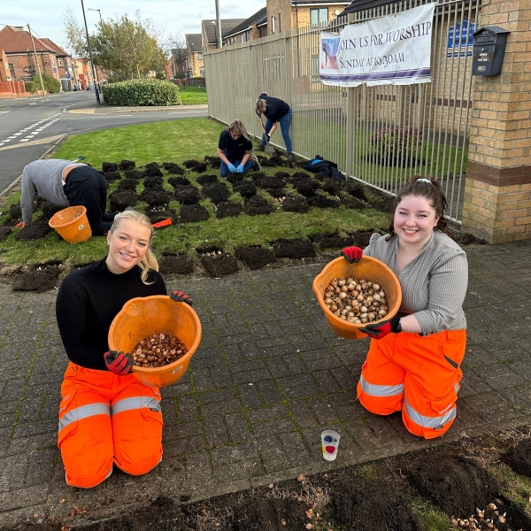 Two girls knelt down holding buckets of bulbs.