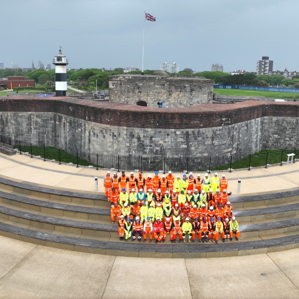 Group of men and women in hi-vis orange and yellow workwear stood on steps in front of Southsea Castle