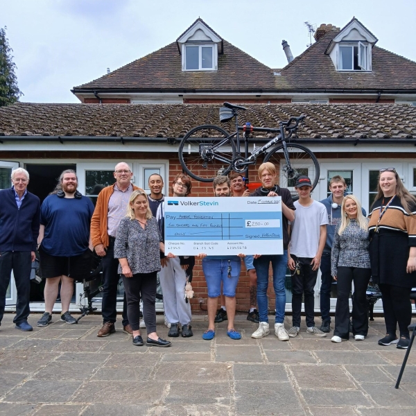 Picture of a group of people stood around a prop check and holding a bike above their heads.