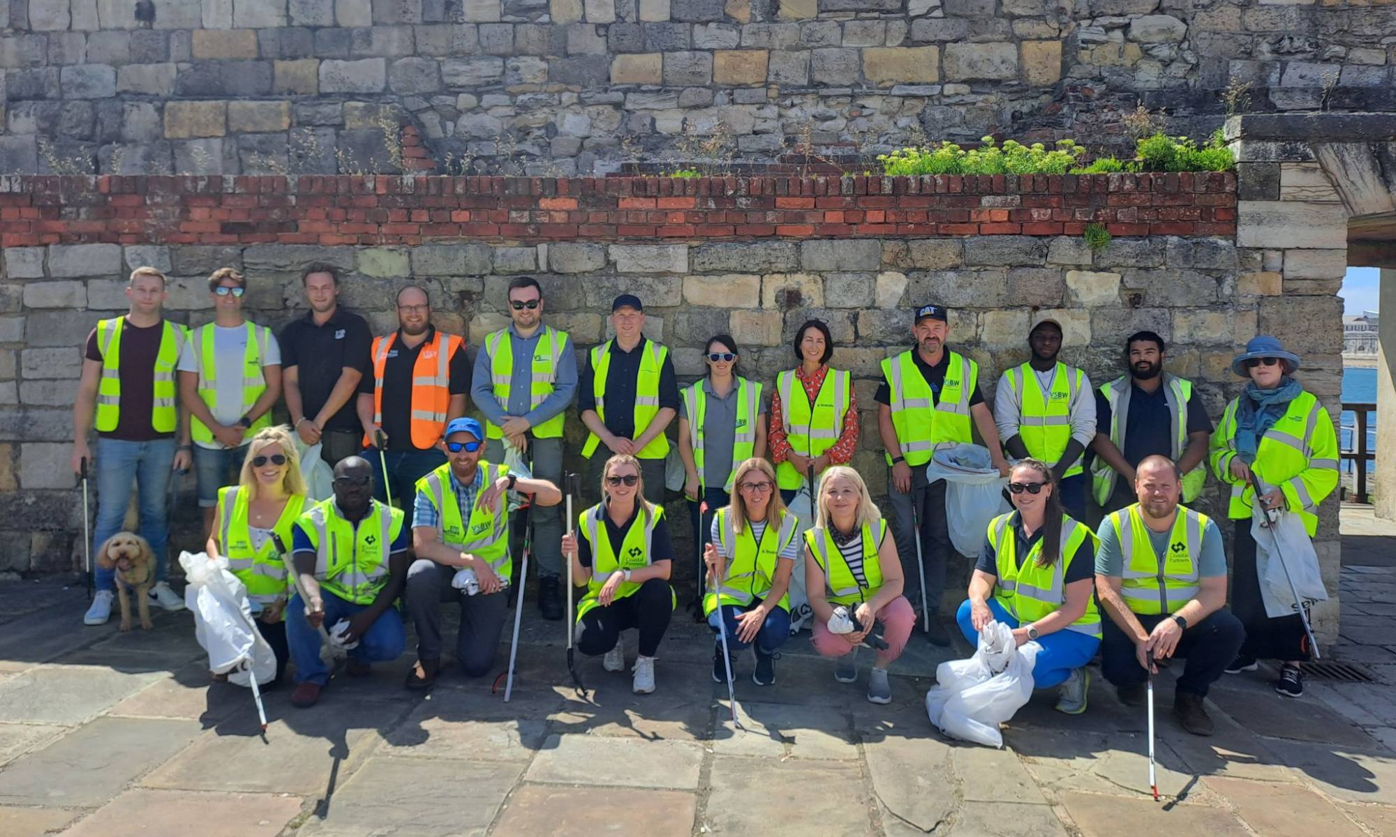 Group picture of men and women stood against a wall with litter bags and wearing hi-vis jackets