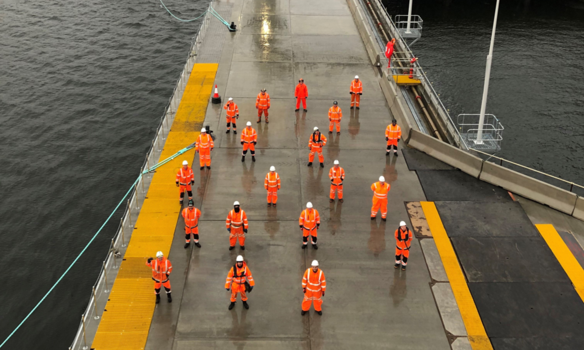 Group of people in orange hi-vis stood on a jetty on the water