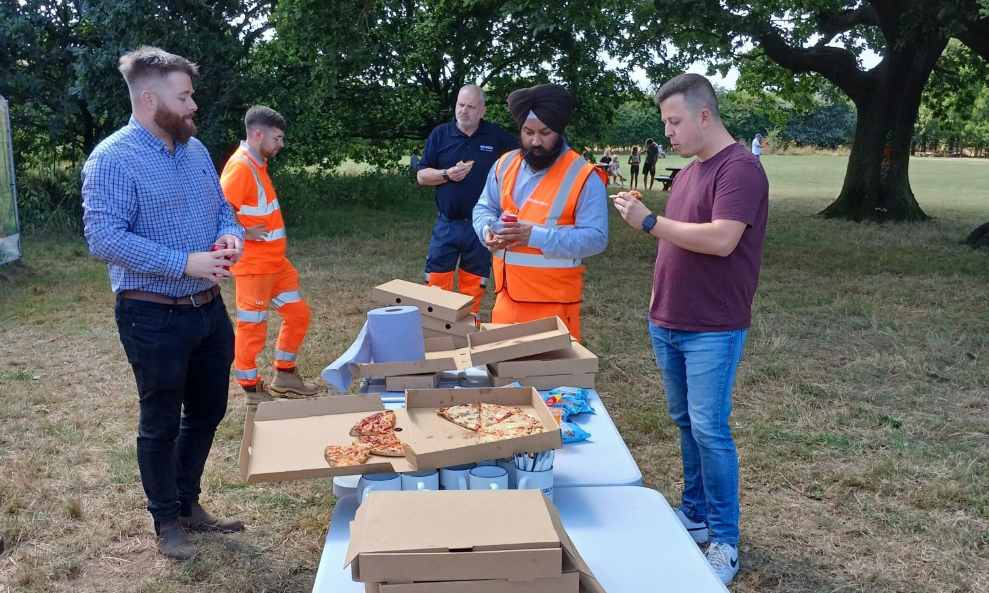 People stood around a table outside eating pizza.
