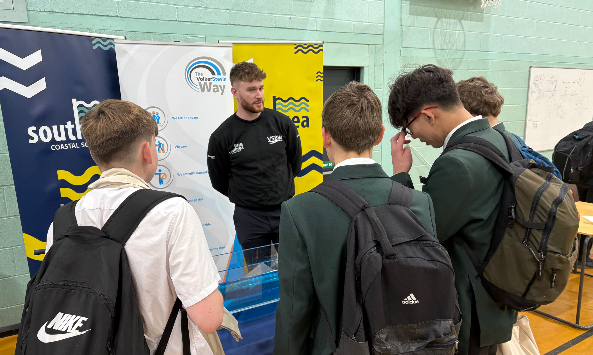 Group of young adults stood by a table taking to a man with a wave machine demonstration