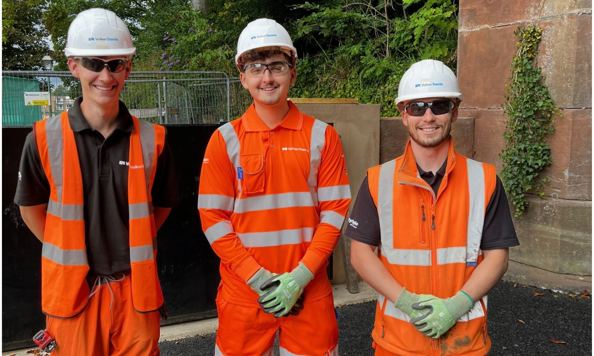 Three men stood together in orange hi-vis workwear, white hard hat and dark safety glasses