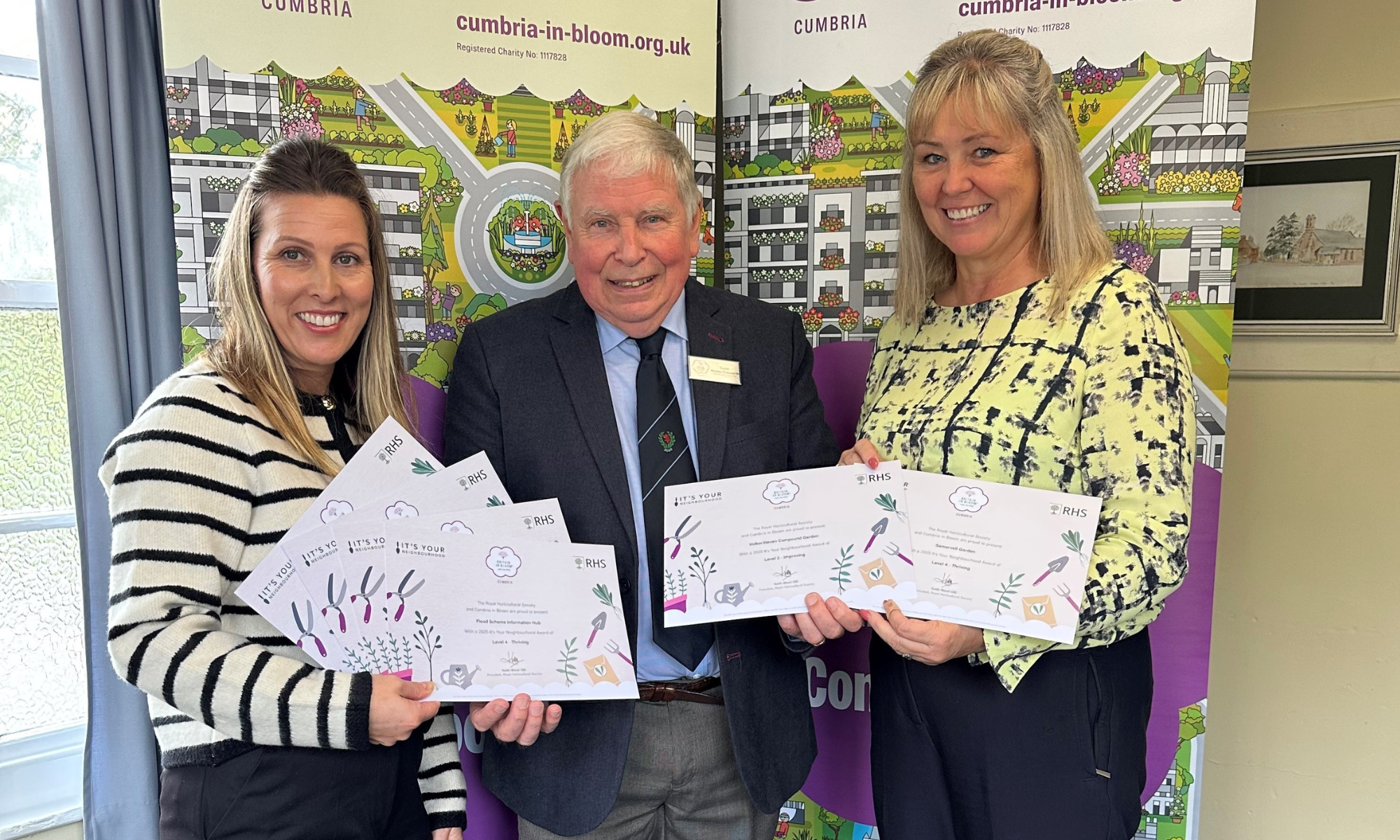 man in suit presenting two women with certificates stood in front of two pull up banners