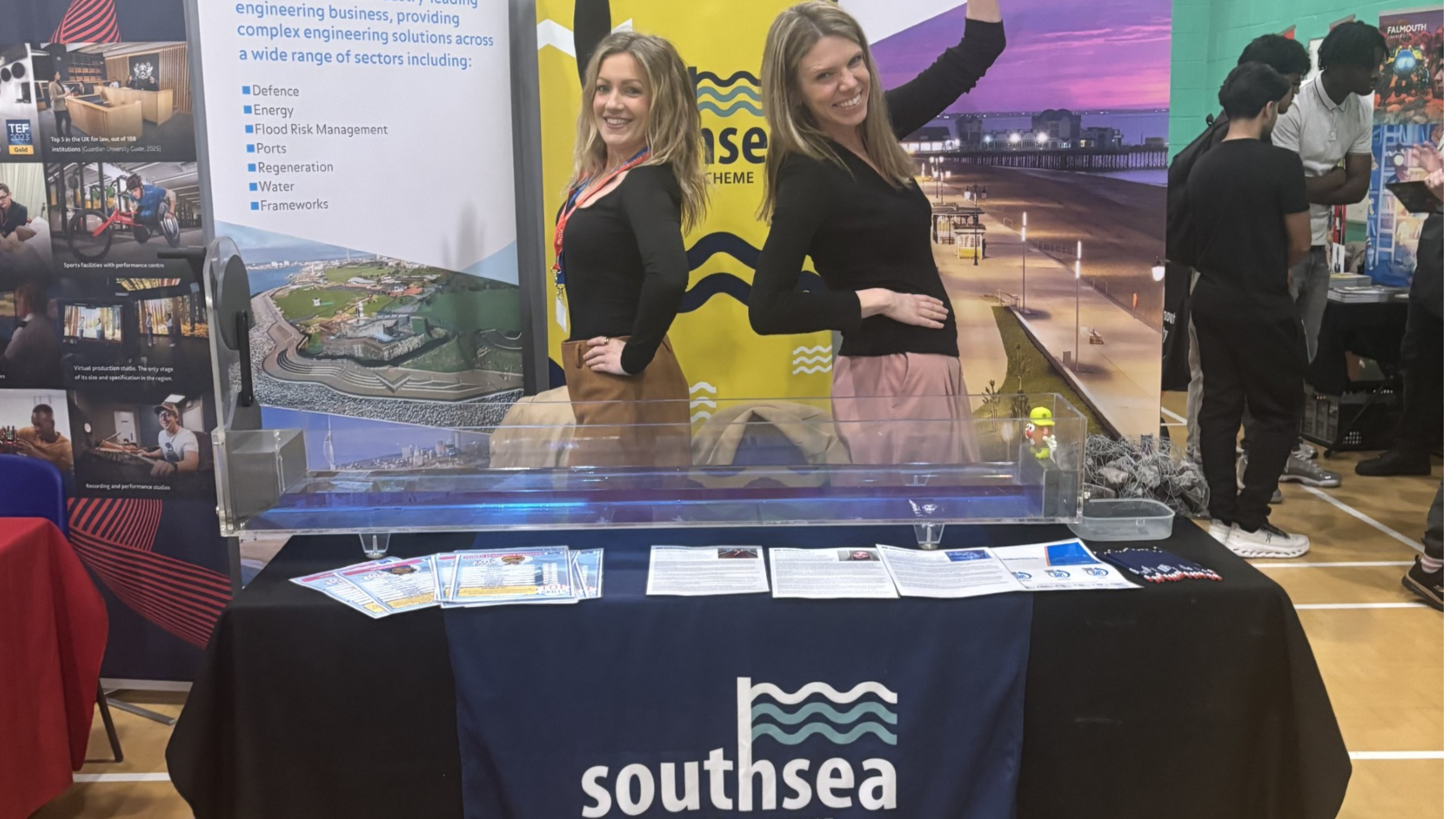 Two women stood behind a table with leaflets on and banners behind them