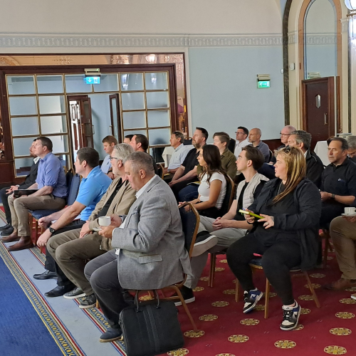 Room of people sat being presented to with slides on a large screen