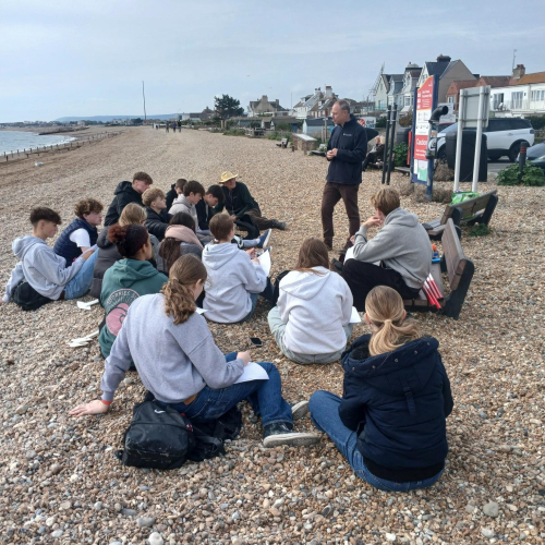Students listening to a talk on a pebble beach.