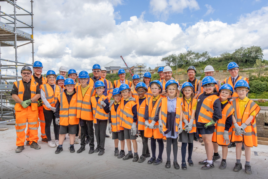 phot of a group of children on a construction site in orange hi-vis jackets and blue hard hats